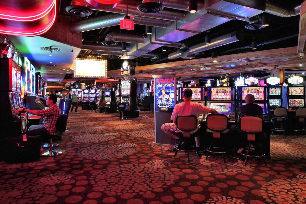 Rows of lit slot machines on a casino floor with a few players seated