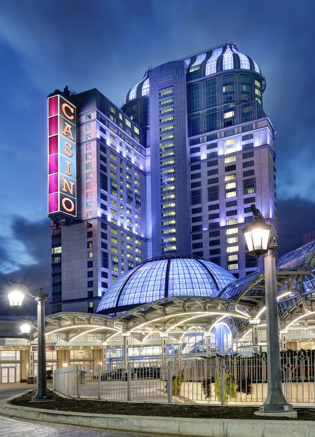 Fallsview Casino Resort hotel tower lit purple at dusk, with a vertical CASINO sign and glass domed entrance