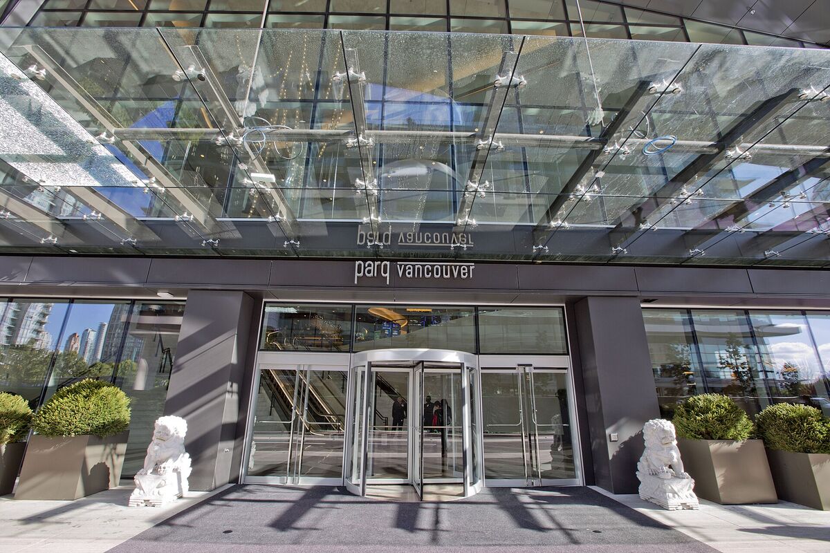 Glass canopy and revolving door entrance of Parq Vancouver, flanked by white stone lion statues